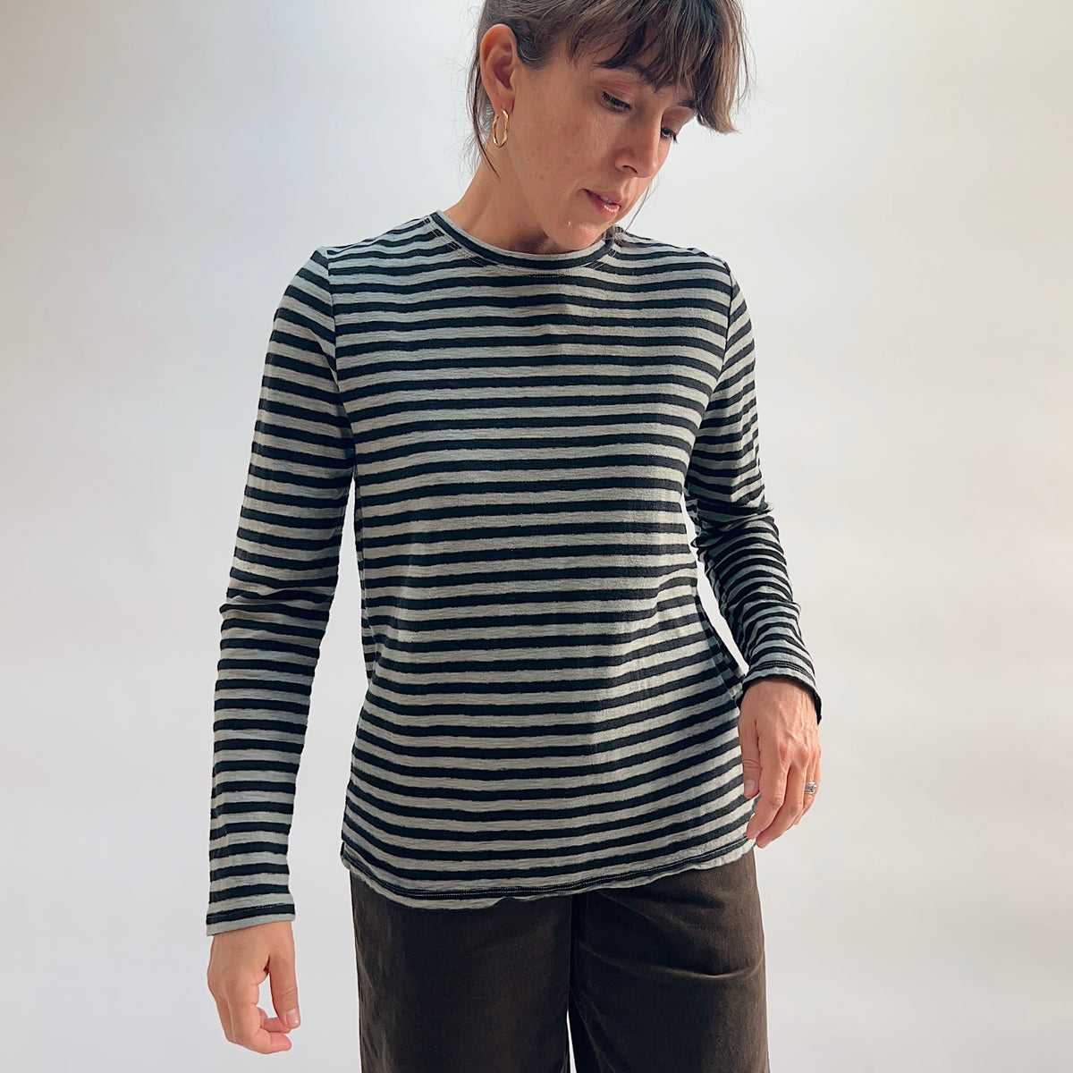 Cut Loose Striped Long Sleeve Easy Tee in Squirrel, black and grey stripe cotton-linen crewneck tee, model looking down, worn with dark wide-leg trousers — three-quarter front view
