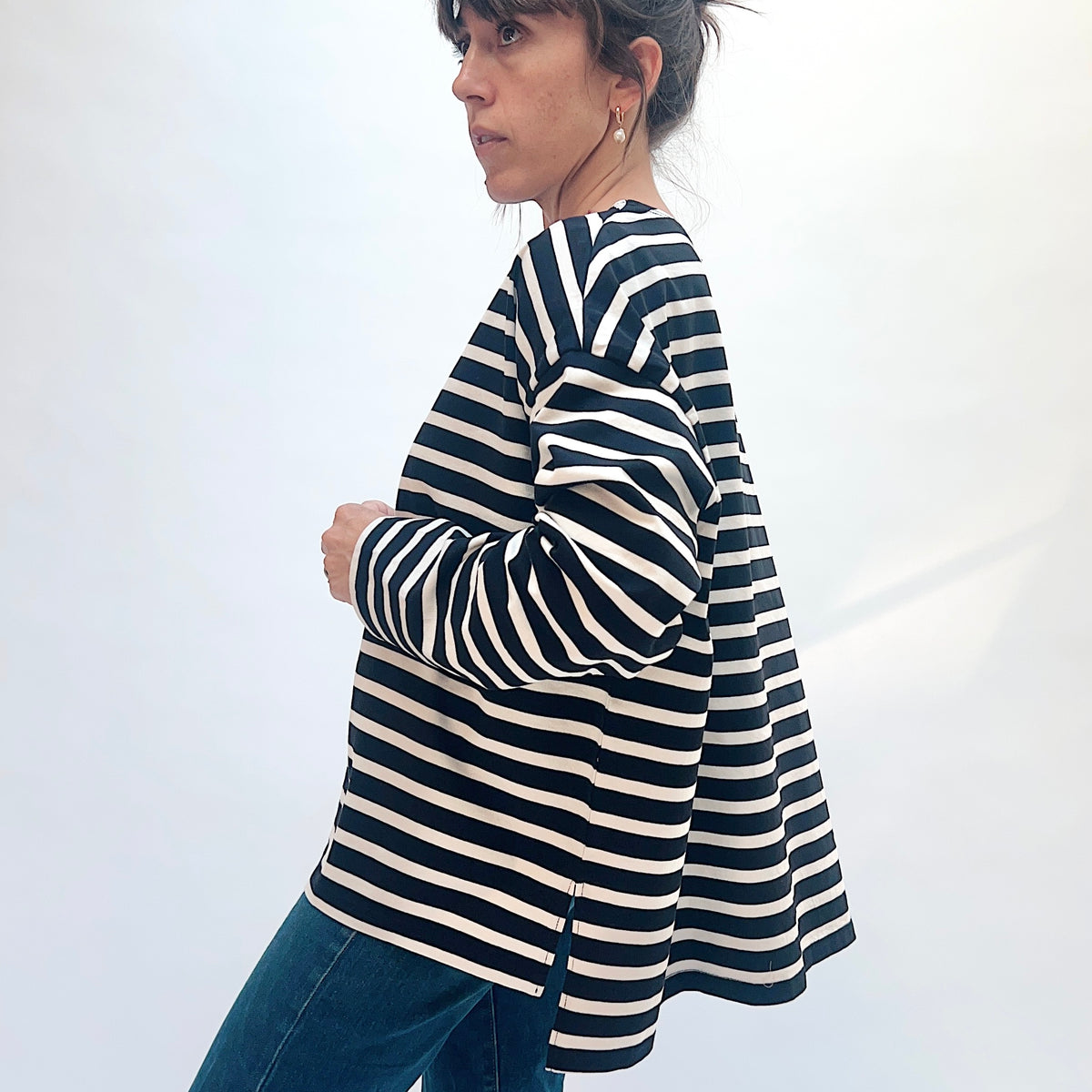 Angled side view of the black and natural striped knit pullover, showing the sleeve, side slit, and longer back hem.
