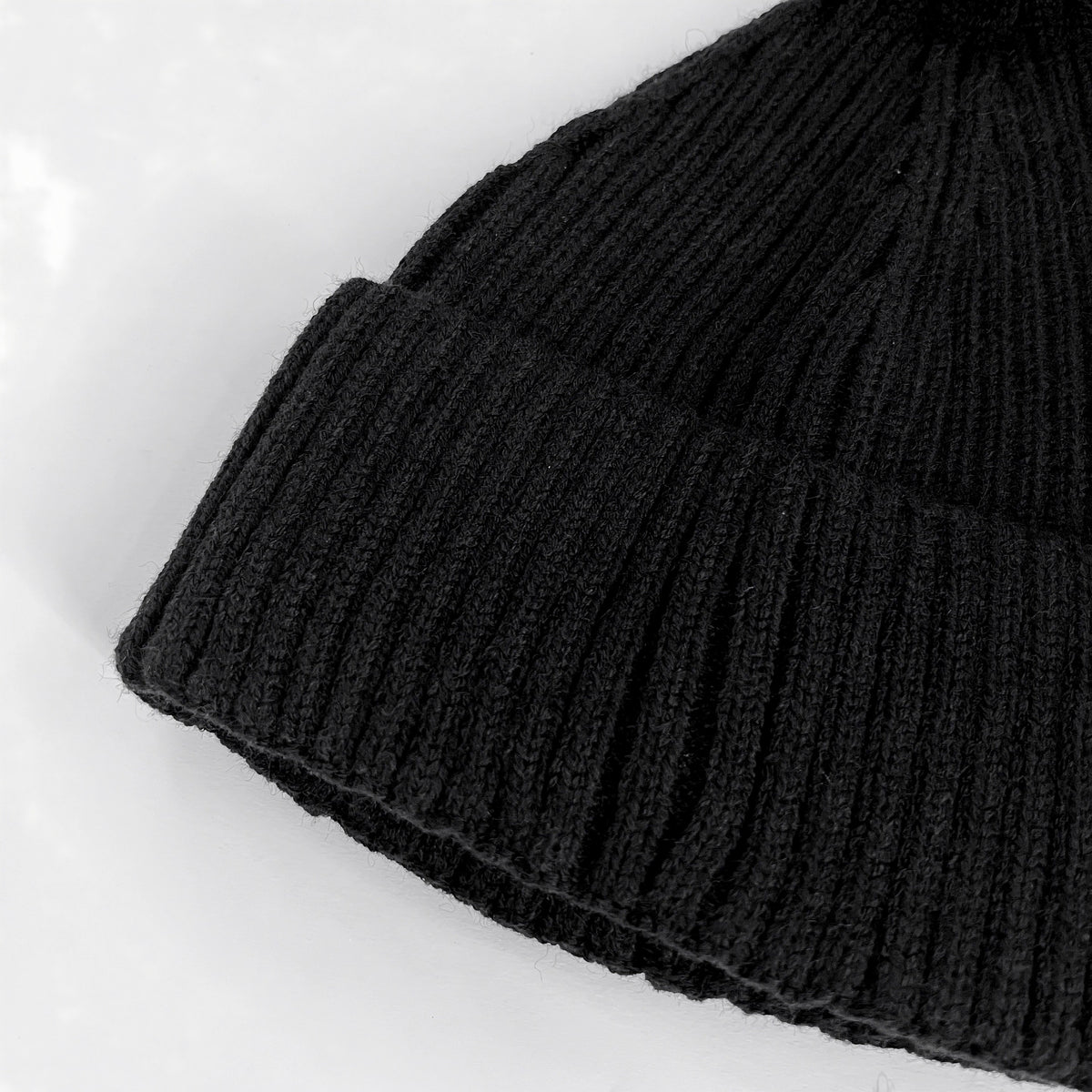 Close-up of the black lambswool beanie showing its ribbed knit texture and folded cuff.
