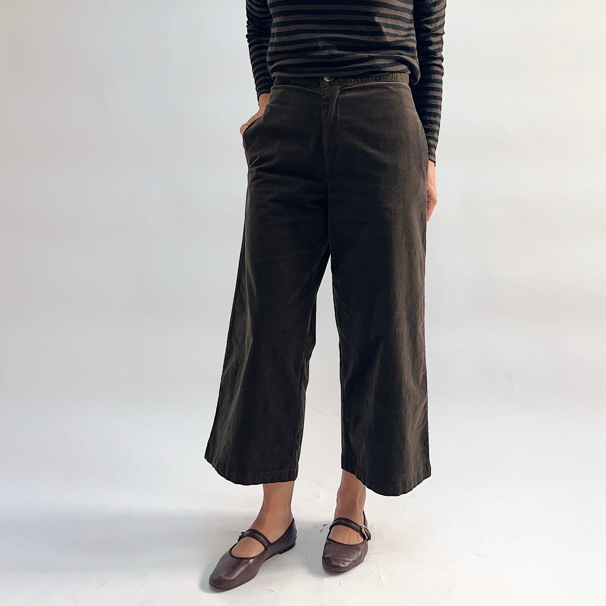 Front view of the Cut Loose Straight Crop Trouser in Chocolate, showing the wide-leg straight silhouette, high waist, front side pockets, and cropped ankle length in rich dark chocolate cotton-spandex twill, paired with brown Mary Jane flats and a striped long-sleeve top
