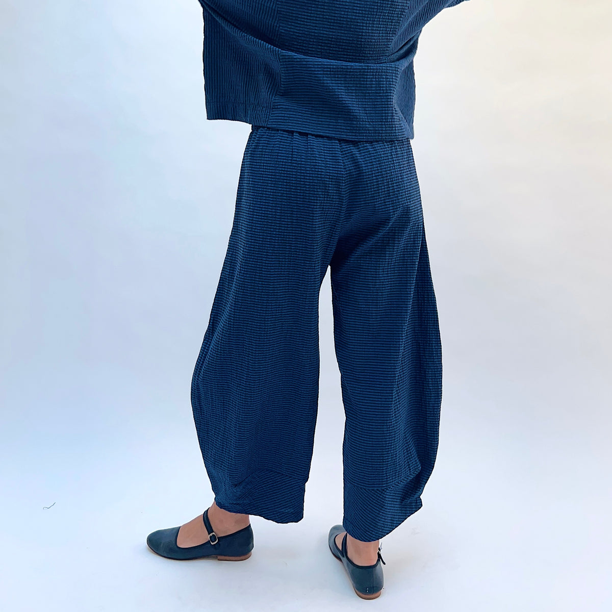 Niche Izzie Pant in Blue Seersucker Stripe, back view showing the wide-leg tapered silhouette and elastic waistband in teal and black seersucker stripe
