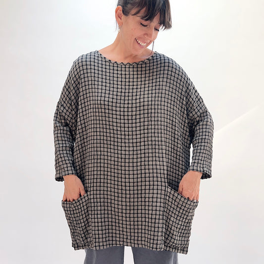Front view of squirrel grid-check crinkle-texture one-size pocket tunic showing scoop neckline with contrast trim, long sleeves, and two front patch pockets, styled with grey wide-leg pants
