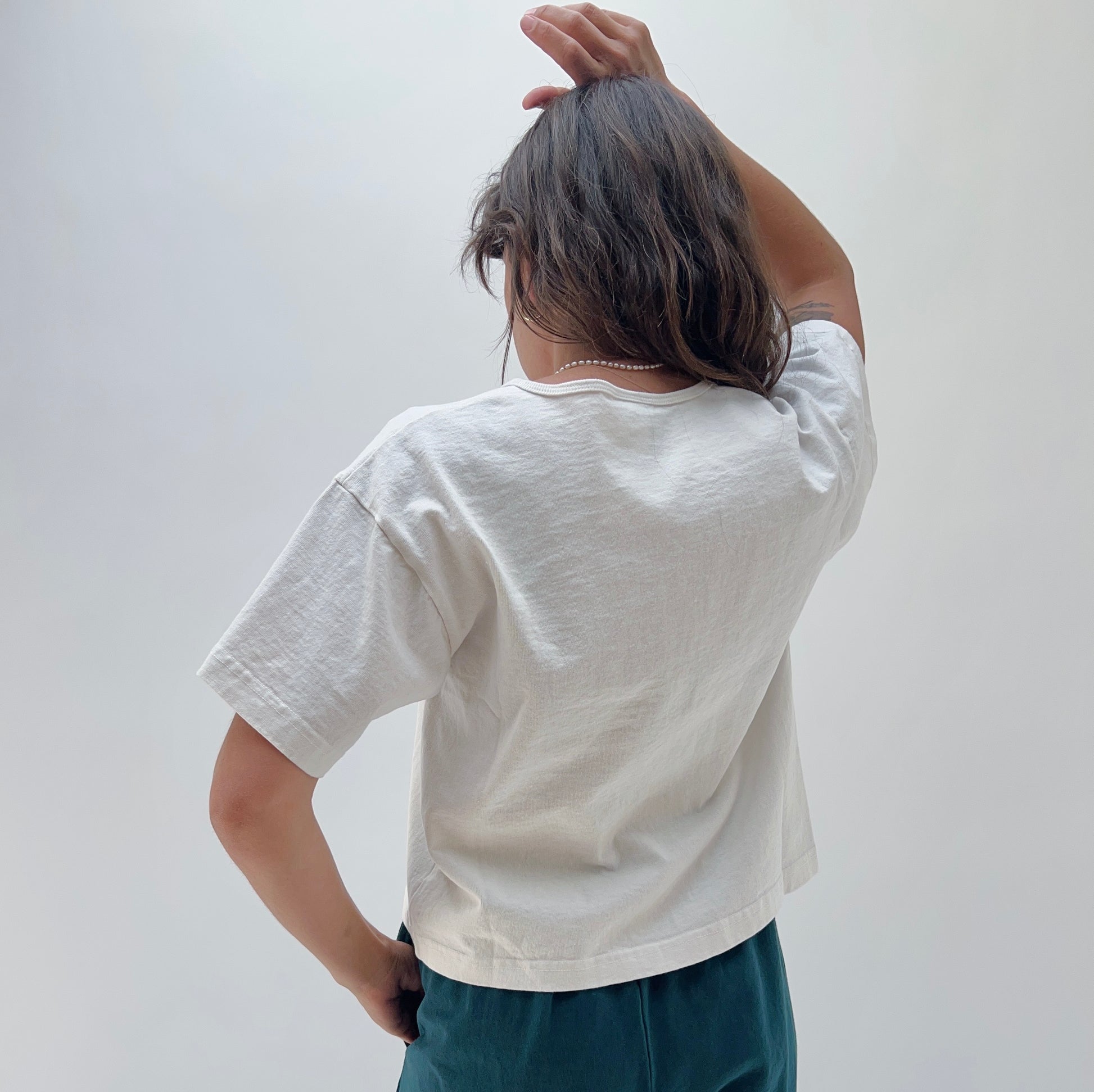 A person wearing a white, short-sleeved, cropped t-shirt and dark pants. The image focus is on the t-shirt.