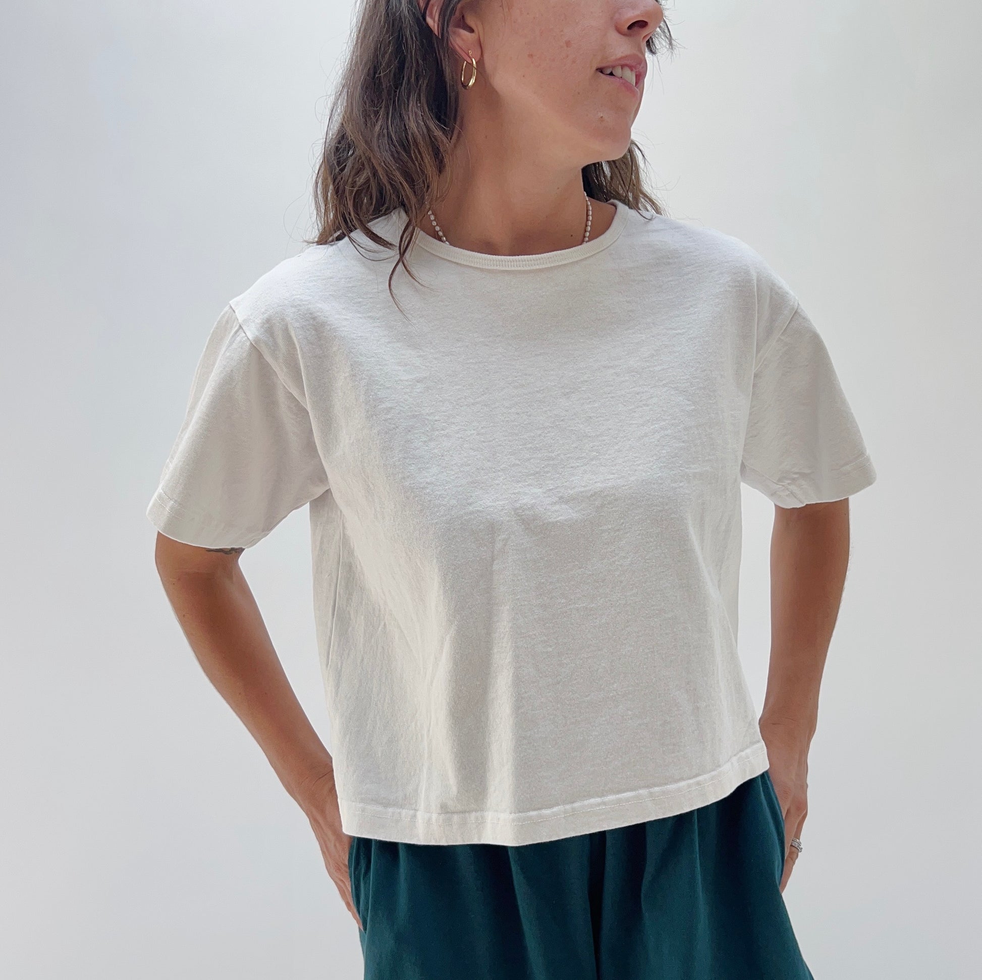 A person wearing a white, short-sleeved, cropped t-shirt and dark pants. The image focus is on the t-shirt.