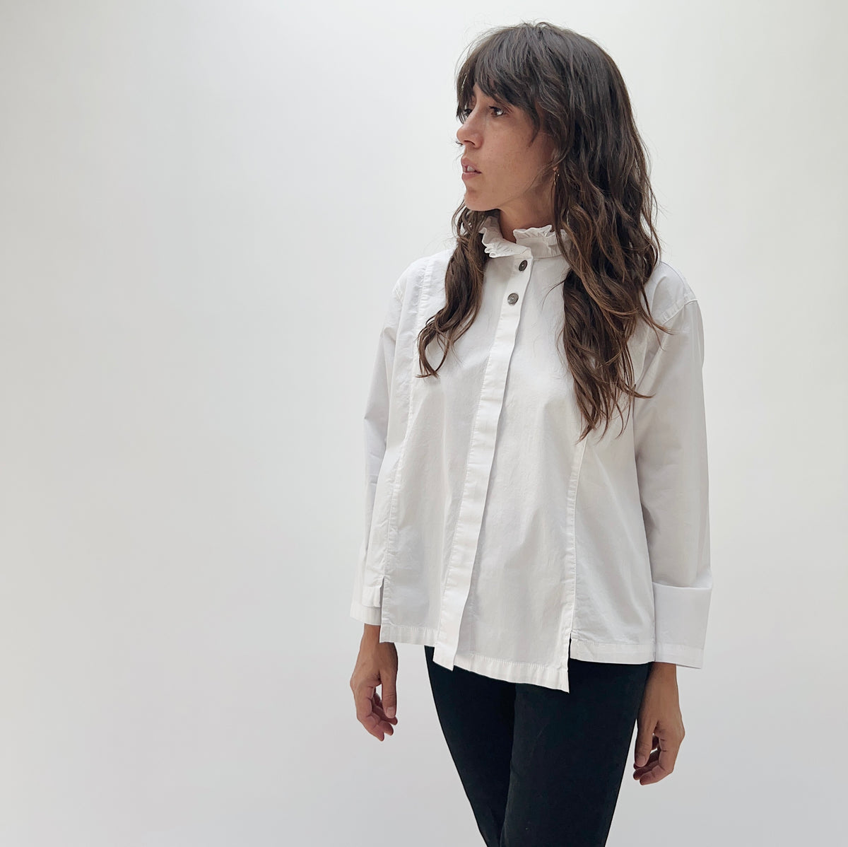 Model wearing the Eleven Stitch Tuxedo Shirt in Chalk, full-length front view, oversized white cotton button-down with ruffled collar and pintuck placket, styled with black pants
