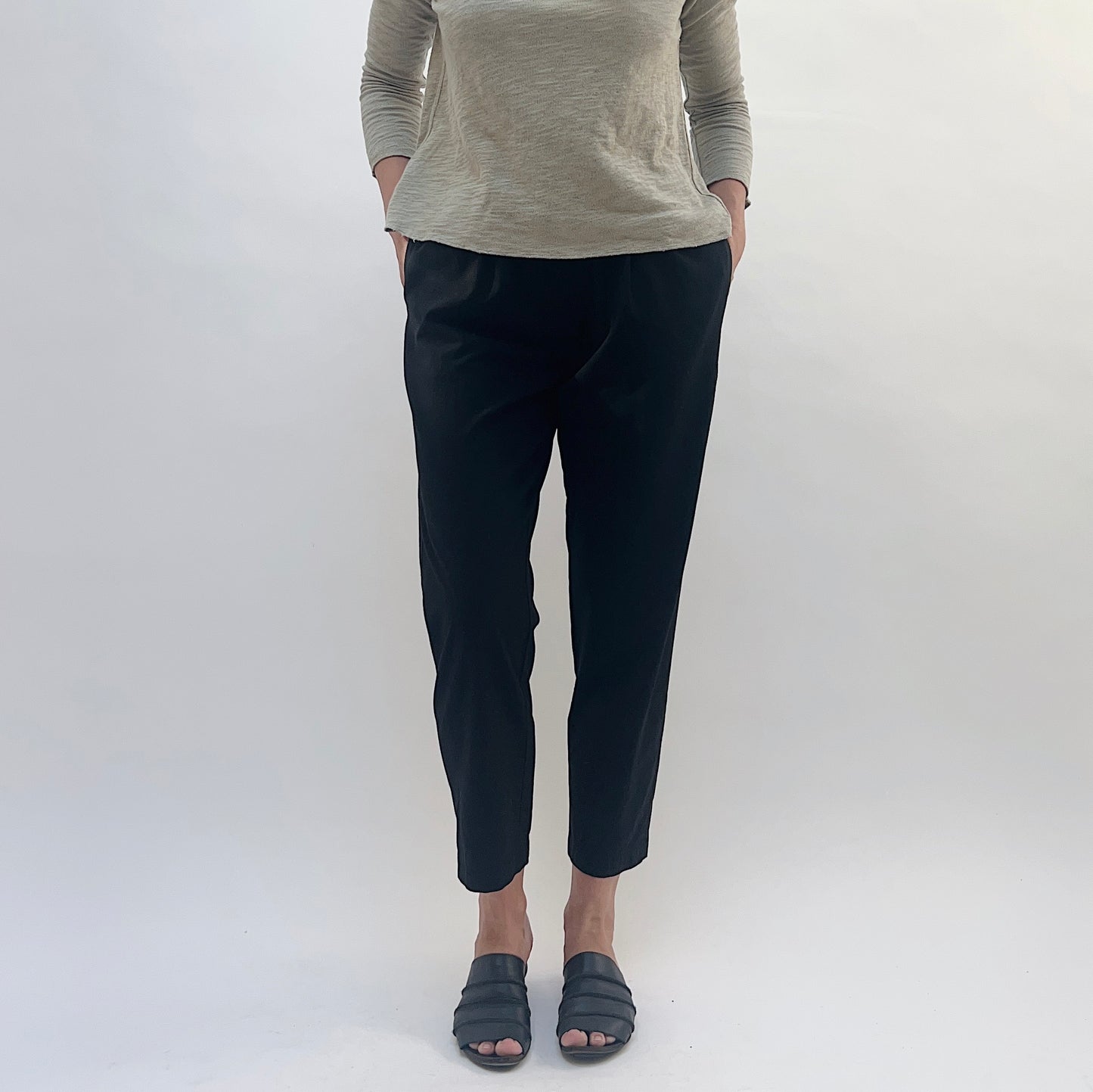 Person wearing black pants and a gray top against a white background