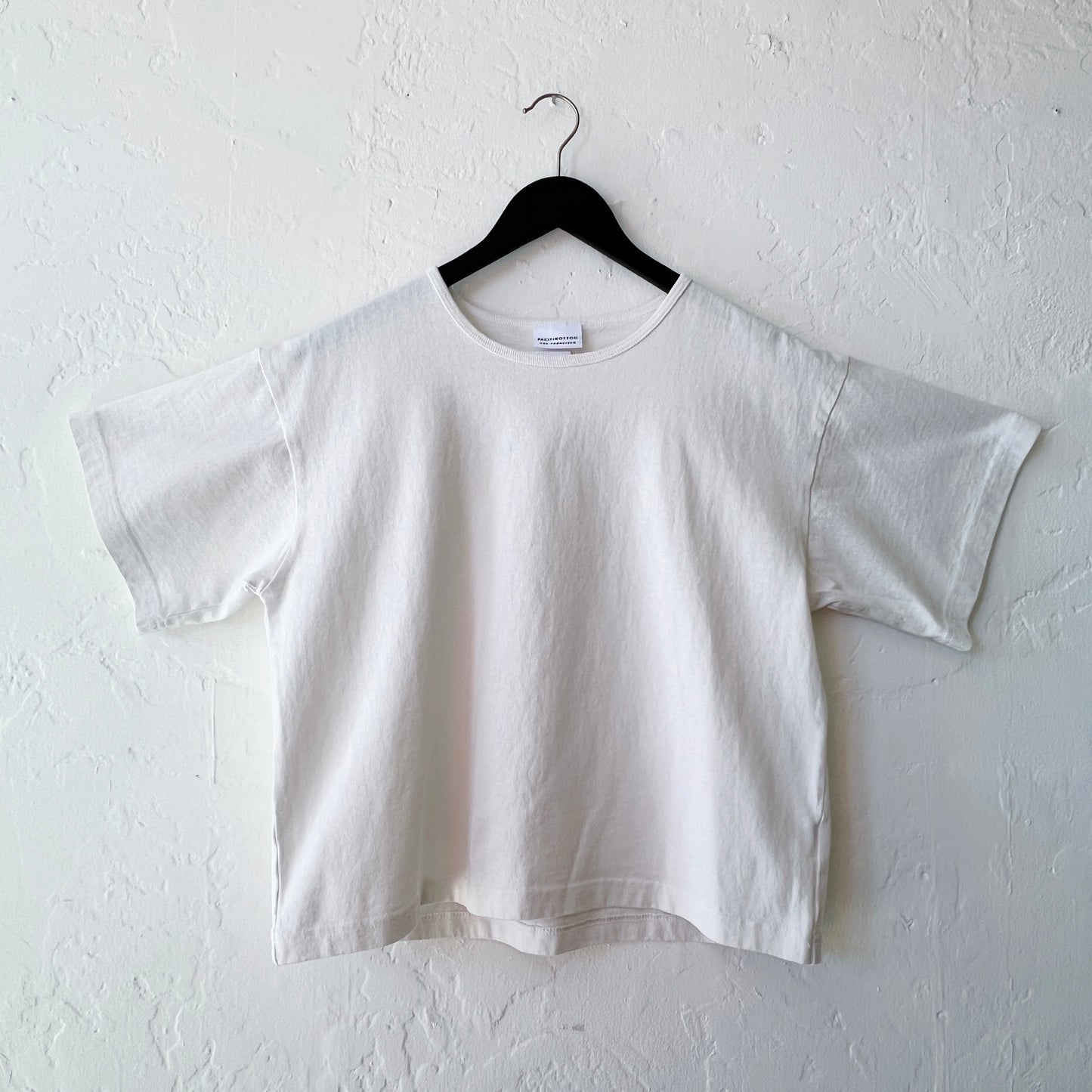 White t-shirt on a hanger against a white wall