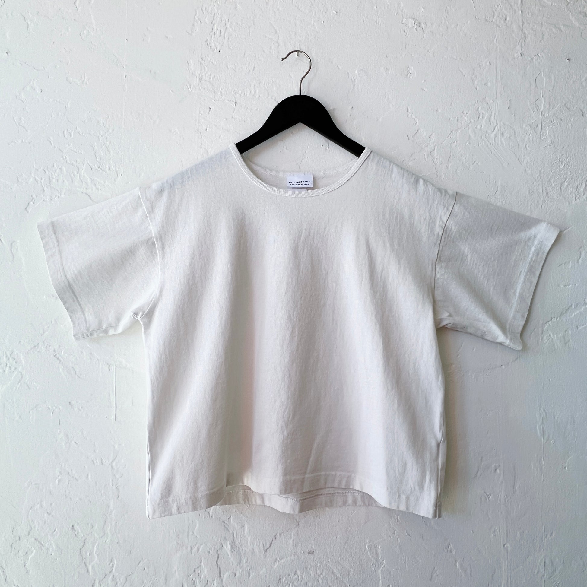 White t-shirt on a hanger against a white wall