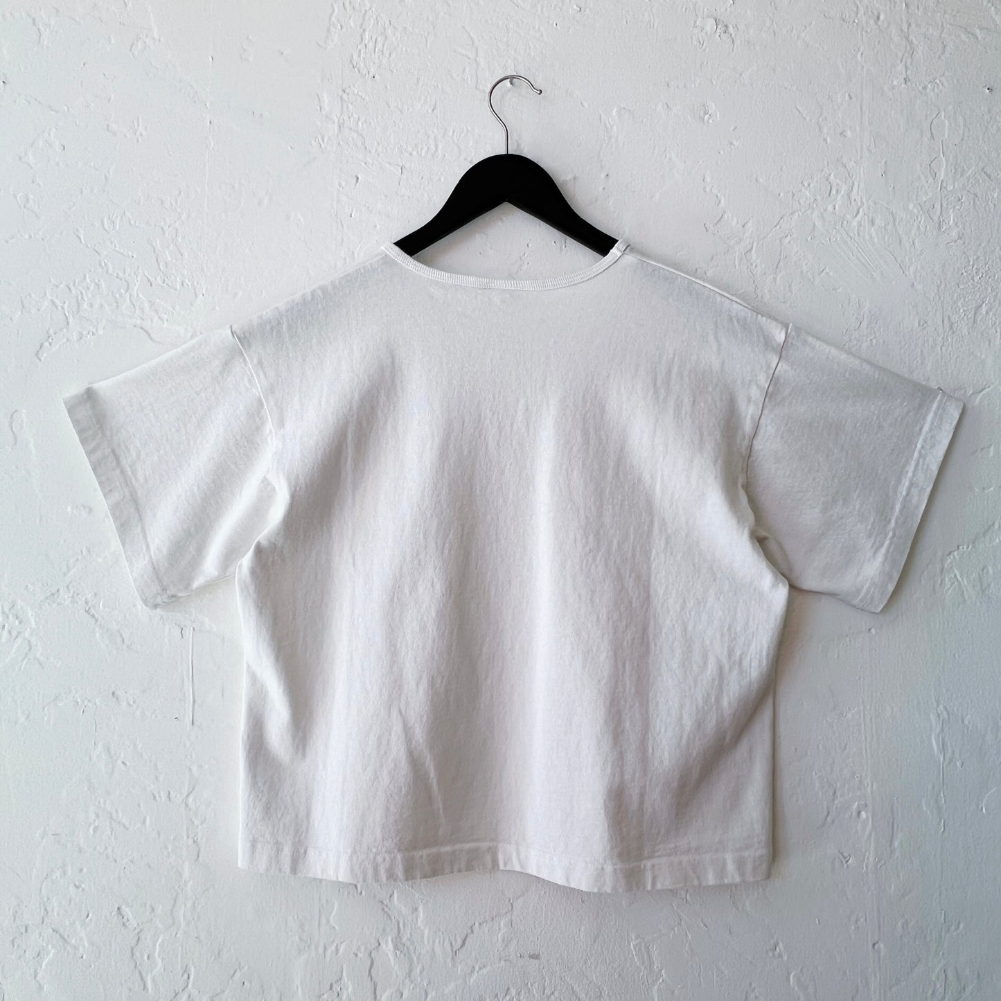 White t-shirt on a black hanger against a white wall