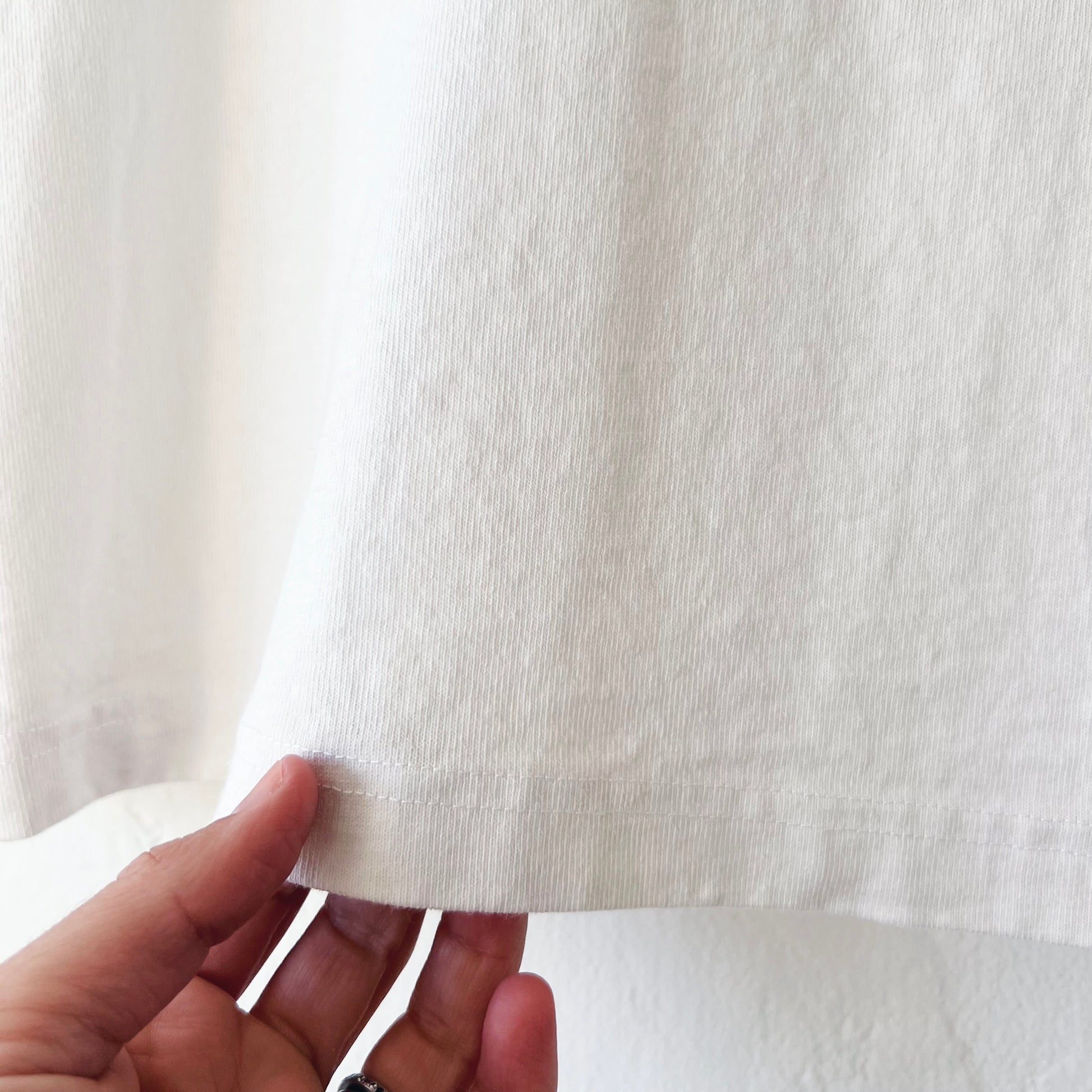 Detail of White t-shirt on a hanger against a white wall