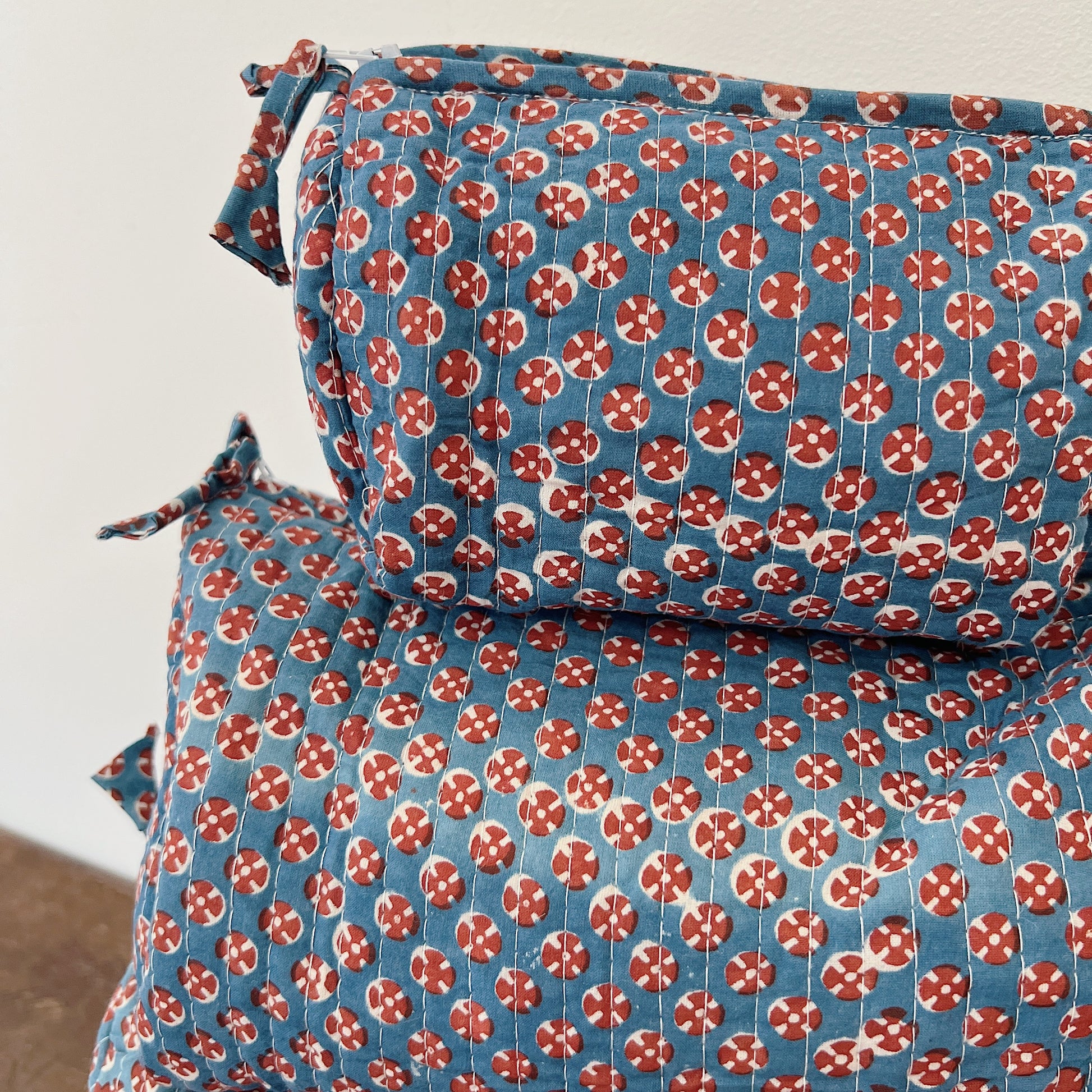 Close-up of the quilted block-print fabric on the toiletry bag, showing the slate blue cotton with red and cream circular motifs and vertical quilting stitches