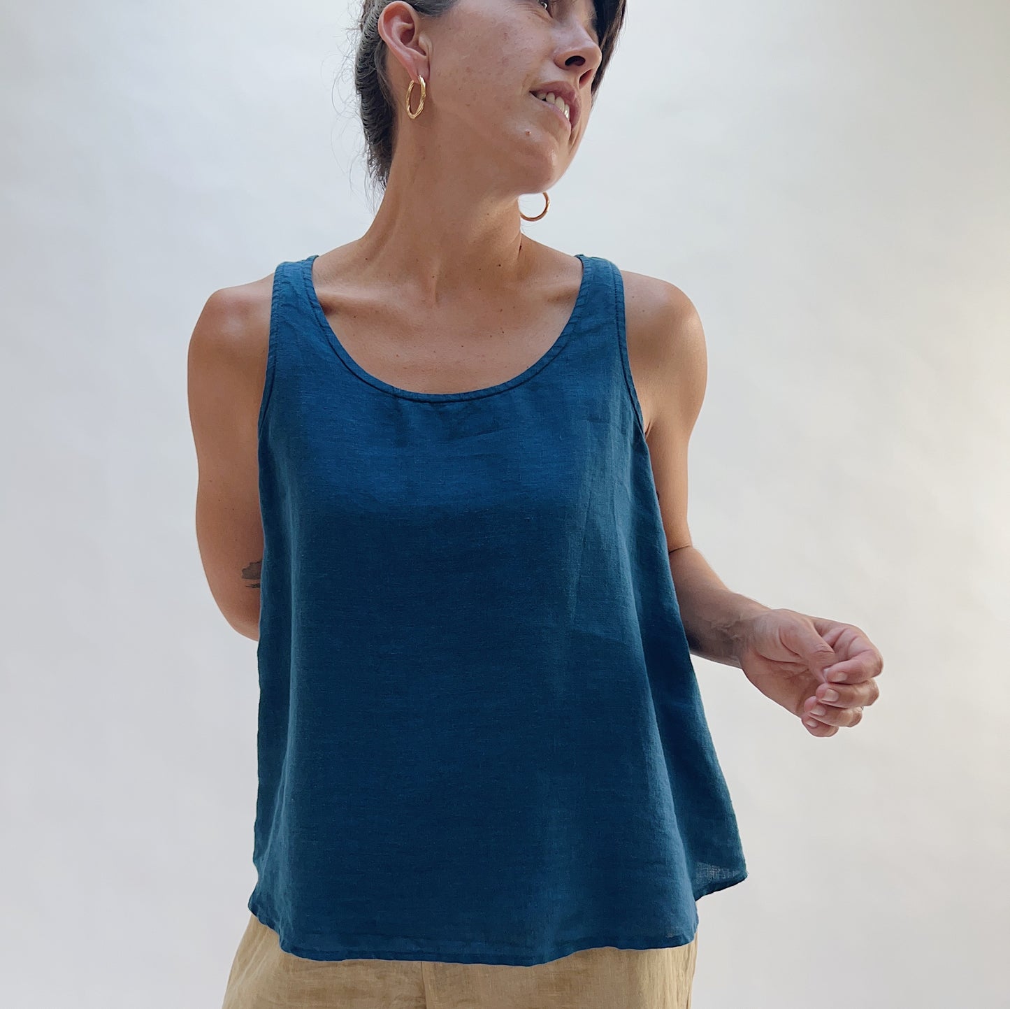 Front three-quarter view of the Basic Tank in French Navy by Yuvita, showing the cropped linen silhouette and scoop neckline in deep teal blue, styled with tan linen trousers