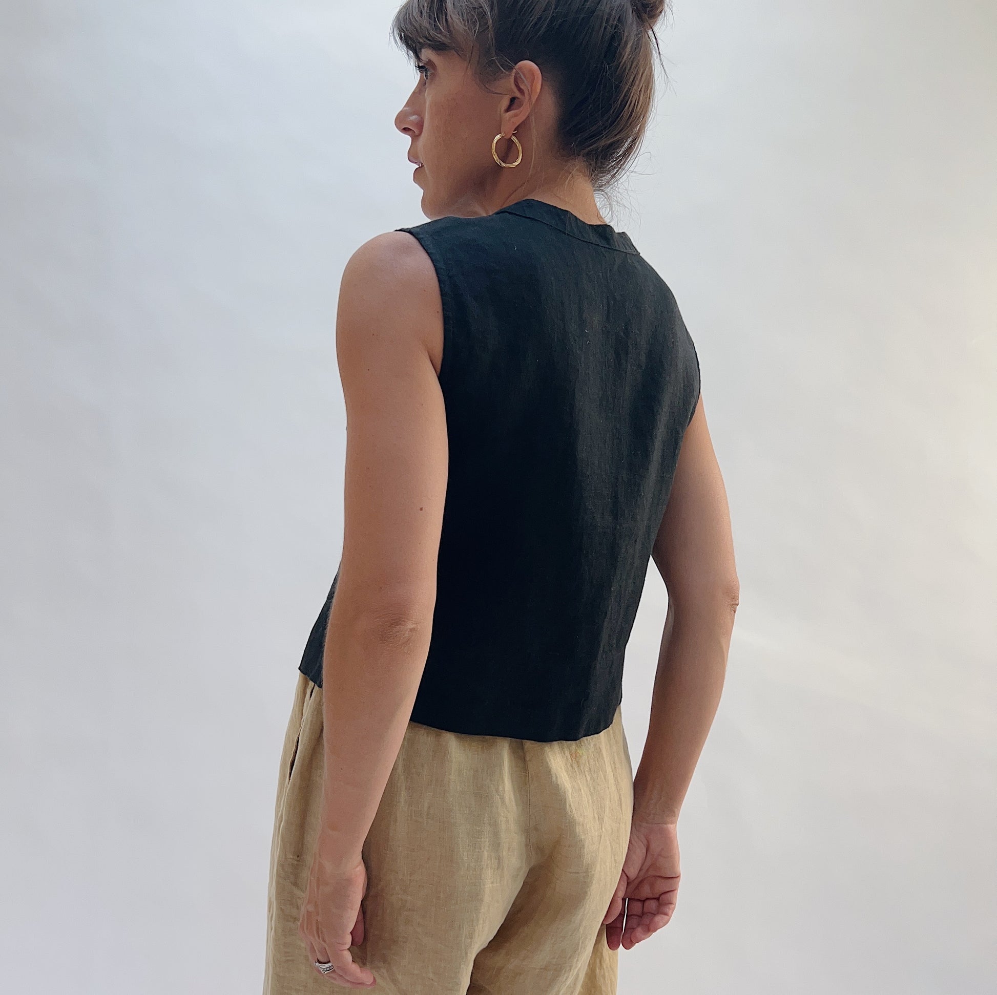 Back view of the Button Front Tank in Black by Yuvita, showing the clean linen back, wide armholes, and cropped hem, styled with tan linen trousers