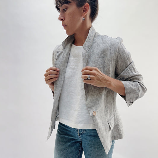 Close-up front view of the Linen Blazer in Grey Pinstripe by Yuvita, showing the open lapel and grey pinstripe linen fabric, styled with a white linen tee and blue jeans