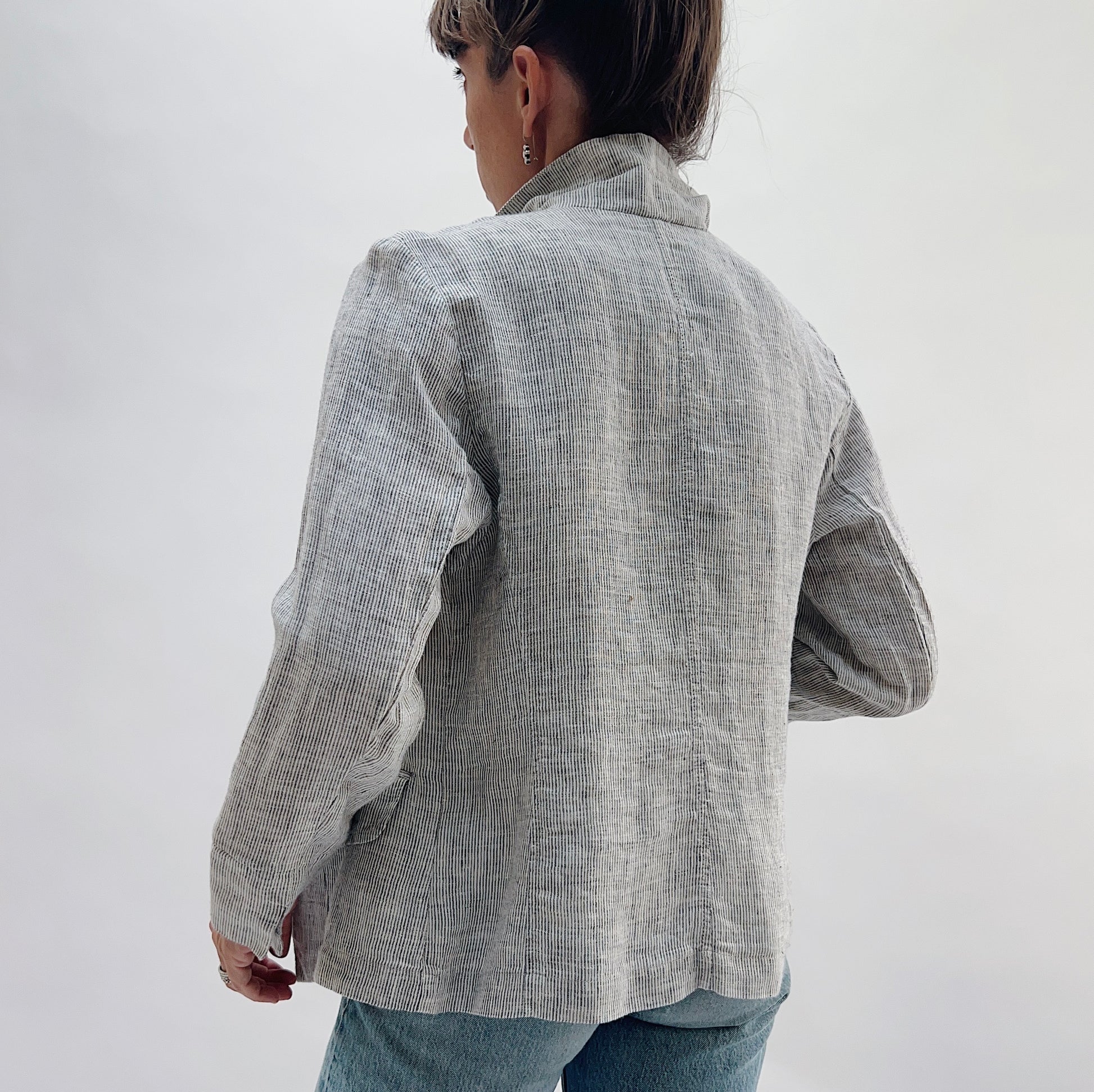 Back view of the Linen Blazer in Grey Pinstripe by Yuvita, showing the clean linen back, structured shoulders, and slightly cropped hem in grey pinstripe, styled with blue jeans