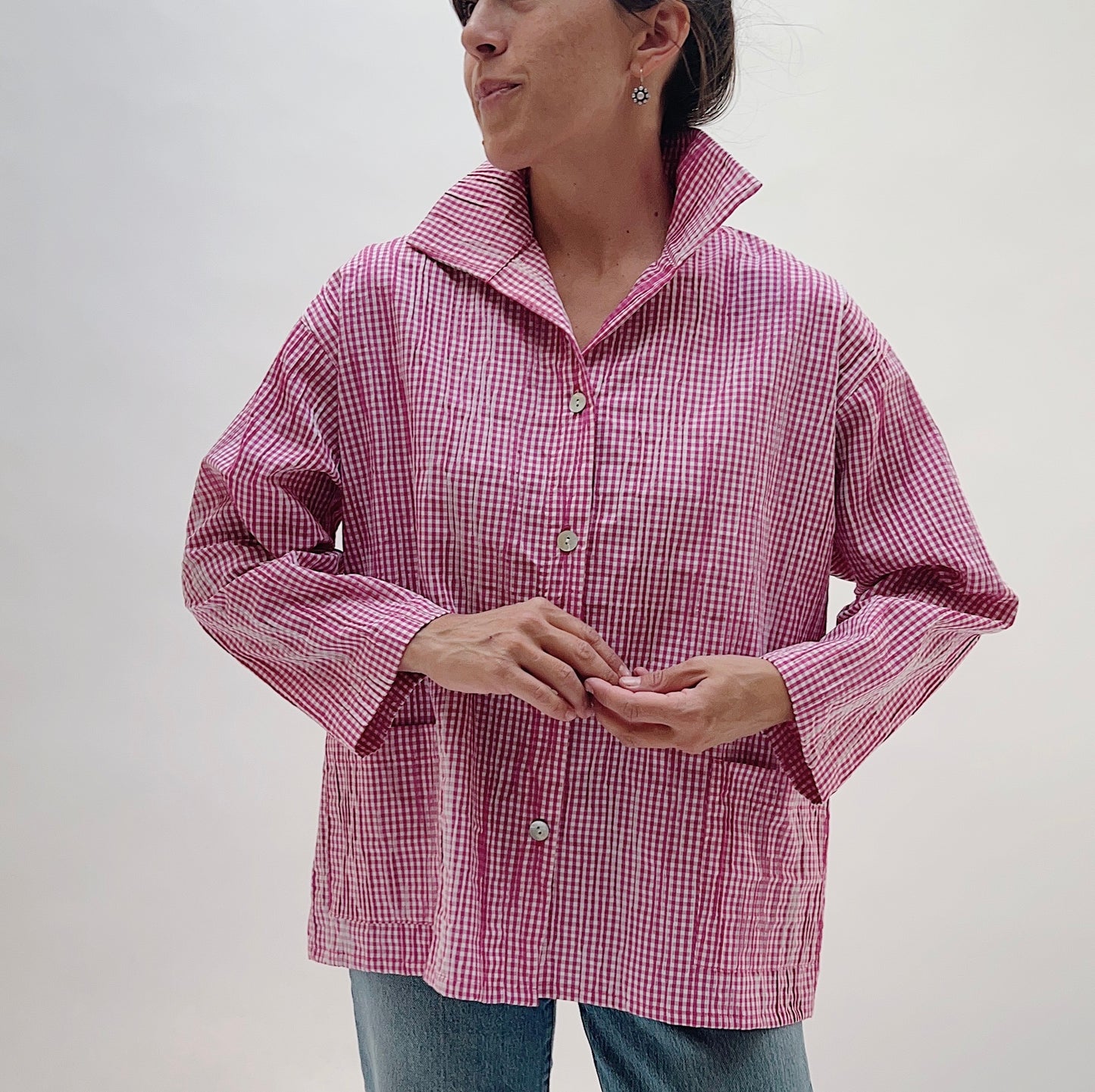 Pink Gingham Button Front Blouse — front view showing pink-and-white mini gingham check, spread collar, three shell buttons, two front patch pockets, and long sleeves, worn with blue jeans on a white background