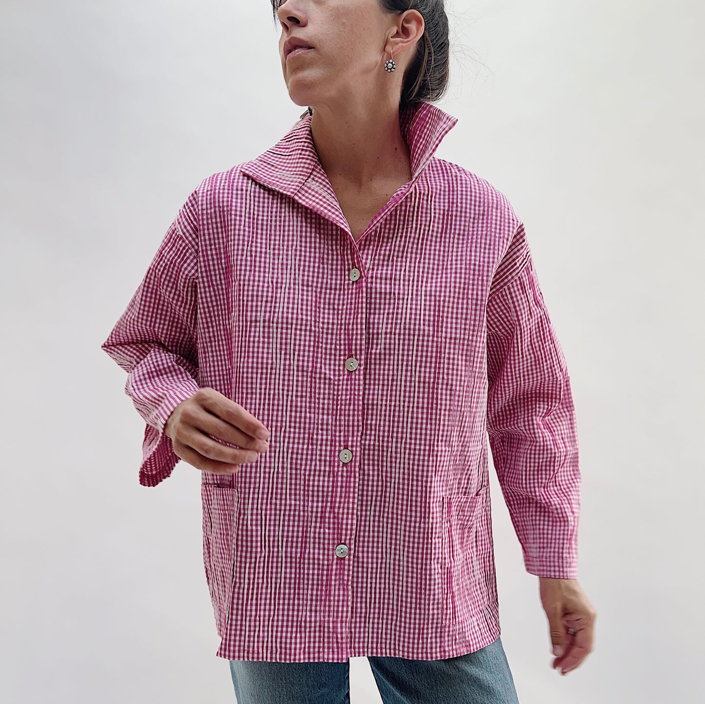 Pink Gingham Button Front Blouse — three-quarter front view showing the relaxed boxy silhouette, spread collar, shell button placket, and one visible front patch pocket, worn with blue jeans on a white background
