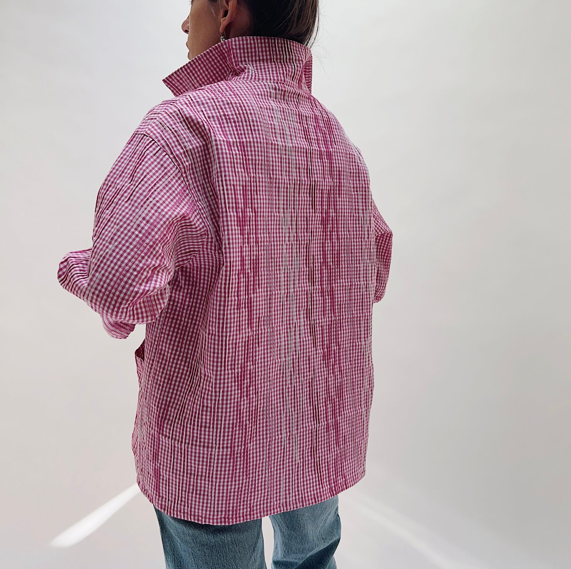 Pink Gingham Button Front Blouse — rear view showing the oversized boxy back, spread collar standing at the neck, and long sleeves with a slight roll, worn with blue jeans on a white background
