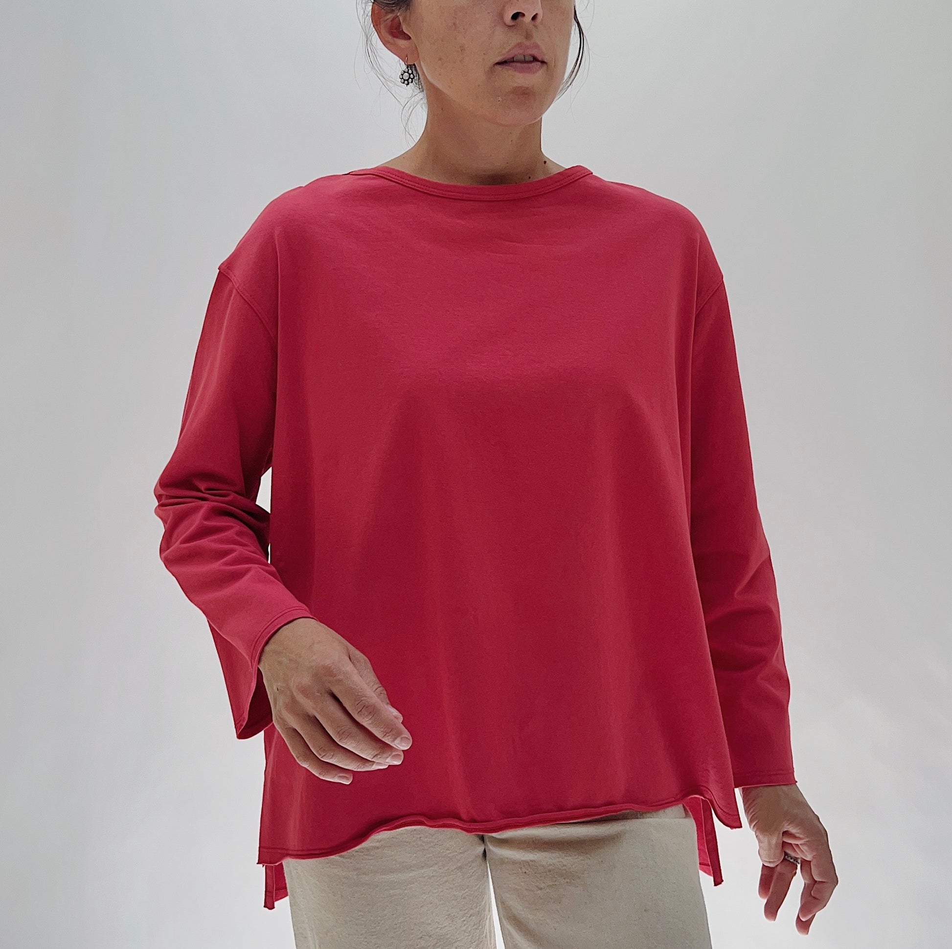 North Star Base Cotton Jersey Beach Tee in Cayenne — front view showing the oversized boxy fit, crew neckline, long sleeves, and curved hem with side slits in cayenne red, worn with cream trousers on a white background