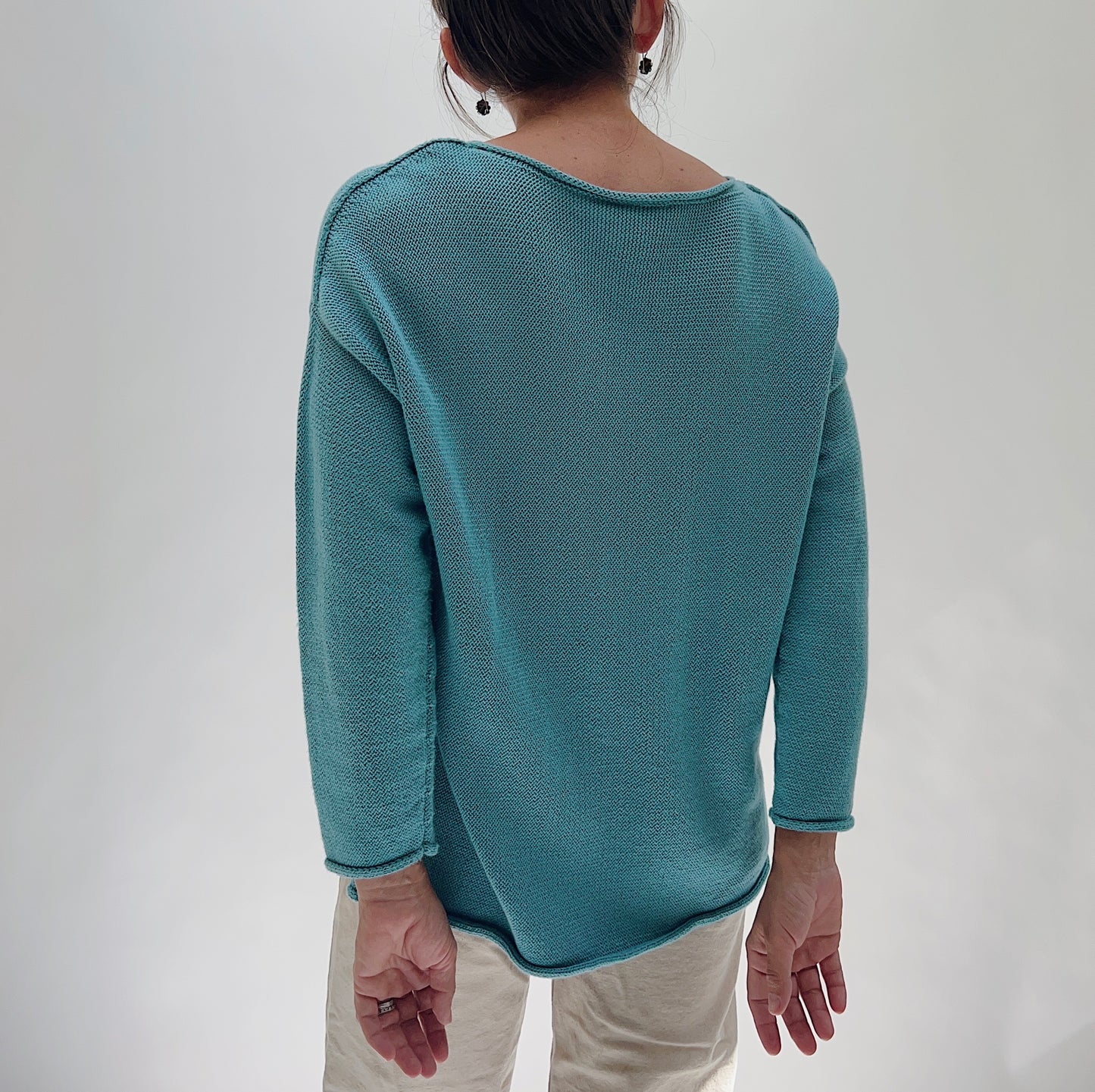 Shannon Passero Handloomed Cotton Emerson Pullover in Tide Blue — rear view showing the smooth open-stitch knit back, wide boat neckline, dropped shoulders, and curved hem, worn with cream trousers on a white background