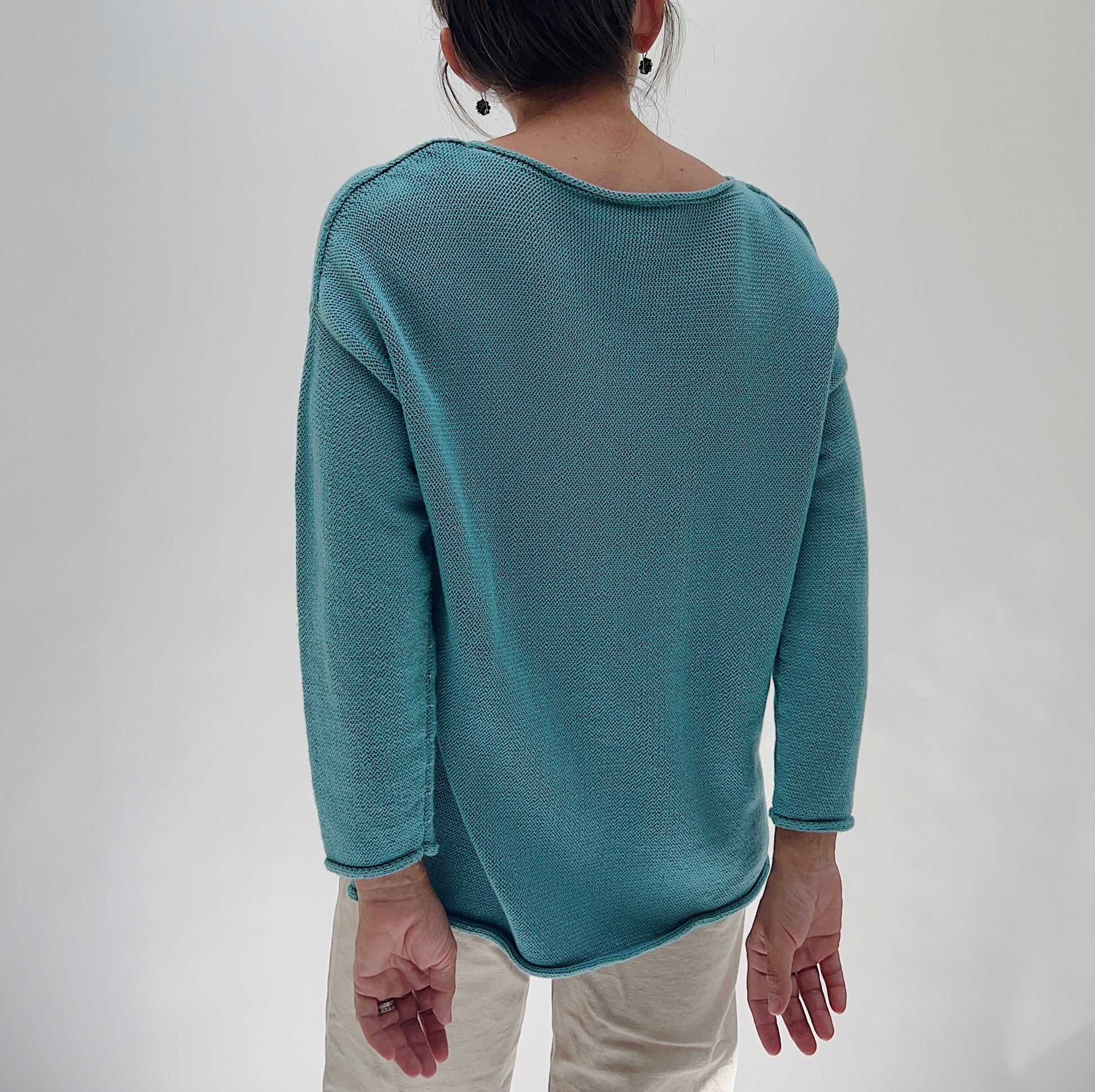Shannon Passero Handloomed Cotton Emerson Pullover in Tide Blue — rear view showing the smooth open-stitch knit back, wide boat neckline, dropped shoulders, and curved hem, worn with cream trousers on a white background