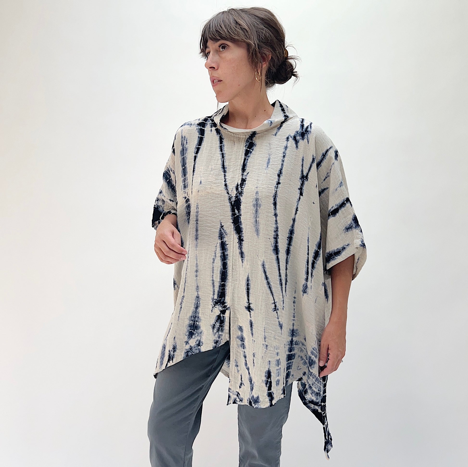 Model wearing the Eleven Stitch one size asymmetrical travel pullover in indigo tie-dye, three-quarter front view showing draped silhouette and asymmetrical hem