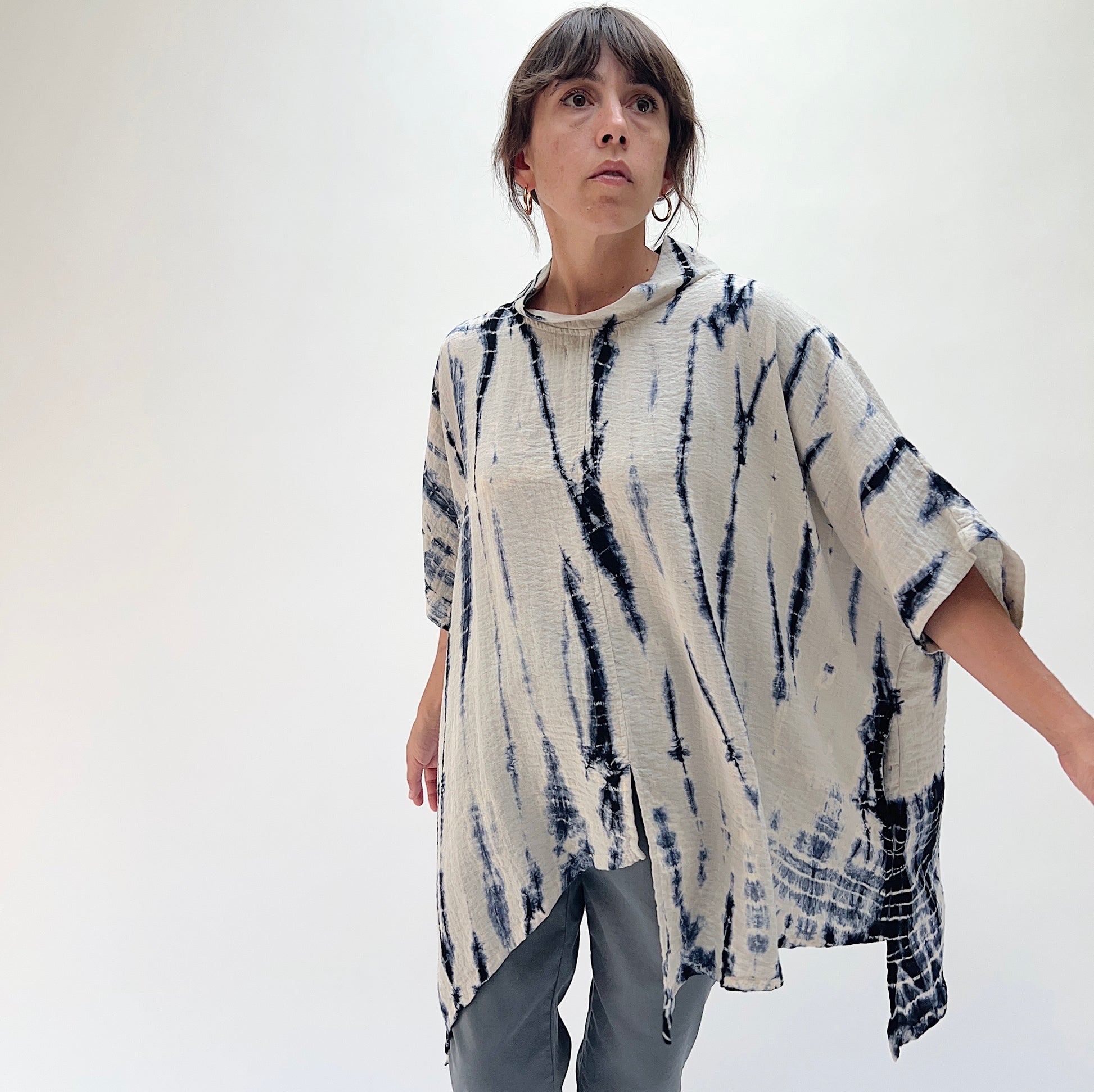 Front view of model in Eleven Stitch indigo tie-dye asymmetrical pullover, showing relaxed oversized fit, mock neck, and pointed hem detail