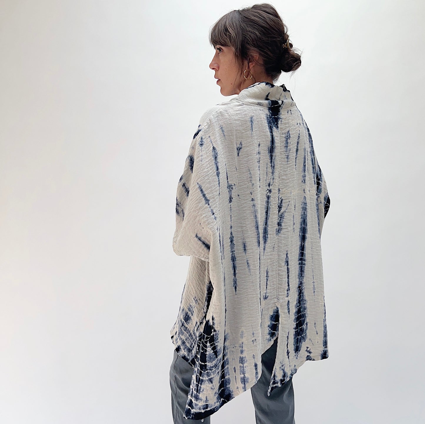 Back view of model wearing Eleven Stitch indigo tie-dye asymmetrical pullover, showing textured fabric, wide sleeves, and elongated back hem against a white background