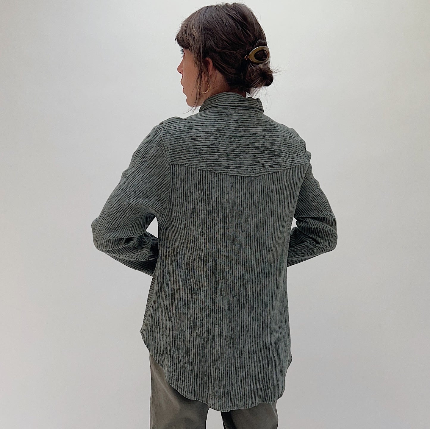 Back view of model wearing Mill Valley Clothing Co olive crinkle-stripe button-down shirt, showing yoke seam detail and curved hem

