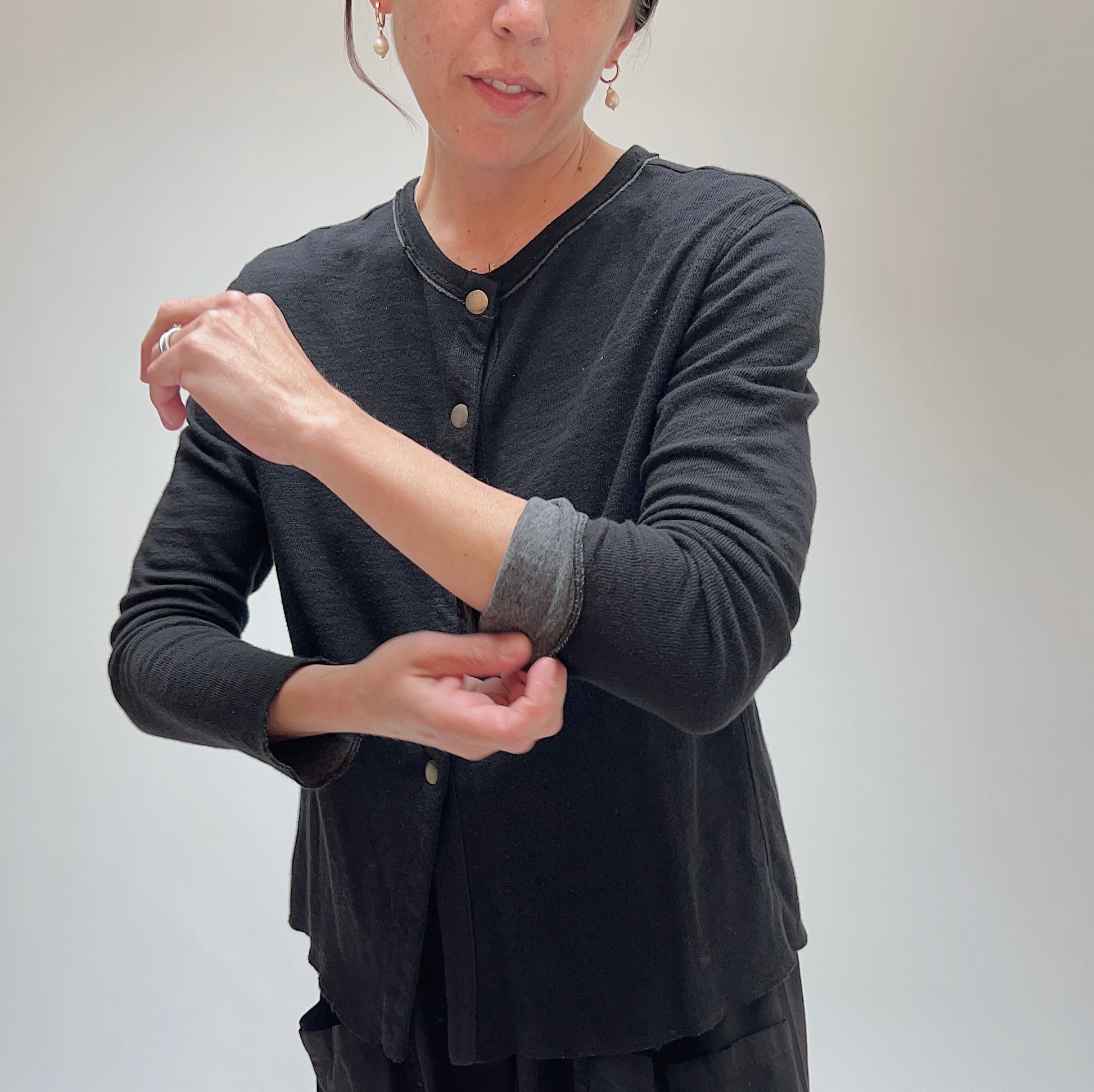 Model rolling the sleeve cuff on the black cardigan, highlighting contrast lining and snap placket detail