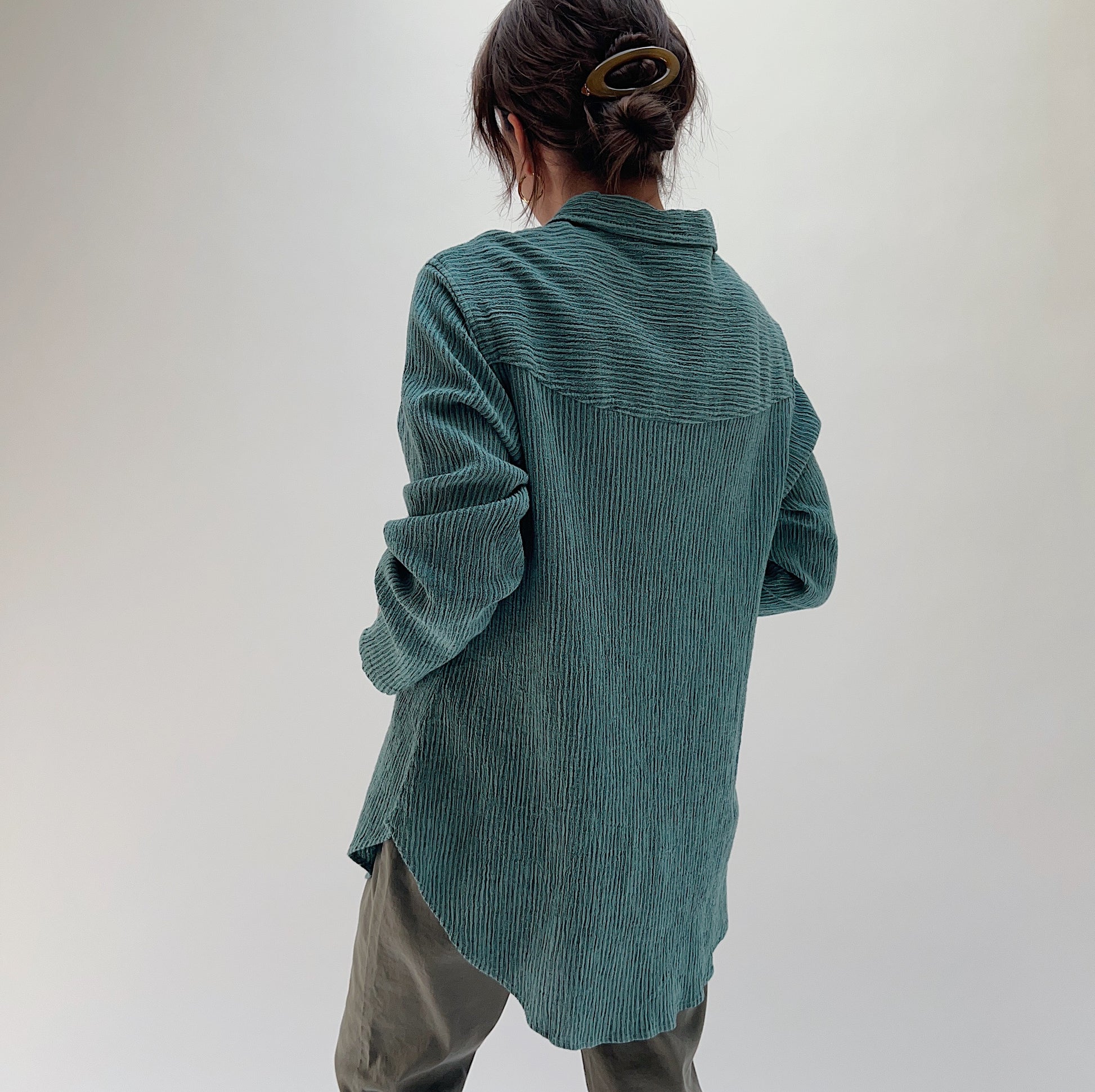 Back view of model wearing Mill Valley Clothing Co blue sage boyfriend button-down, showing yoke seam detail, crinkle-stripe texture, and curved hem