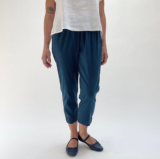 Front view of model wearing Cut Loose dark blue linen-Tencel taper crop pant in Etan, showing elastic waistband, tapered leg, and cropped length at mid-calf