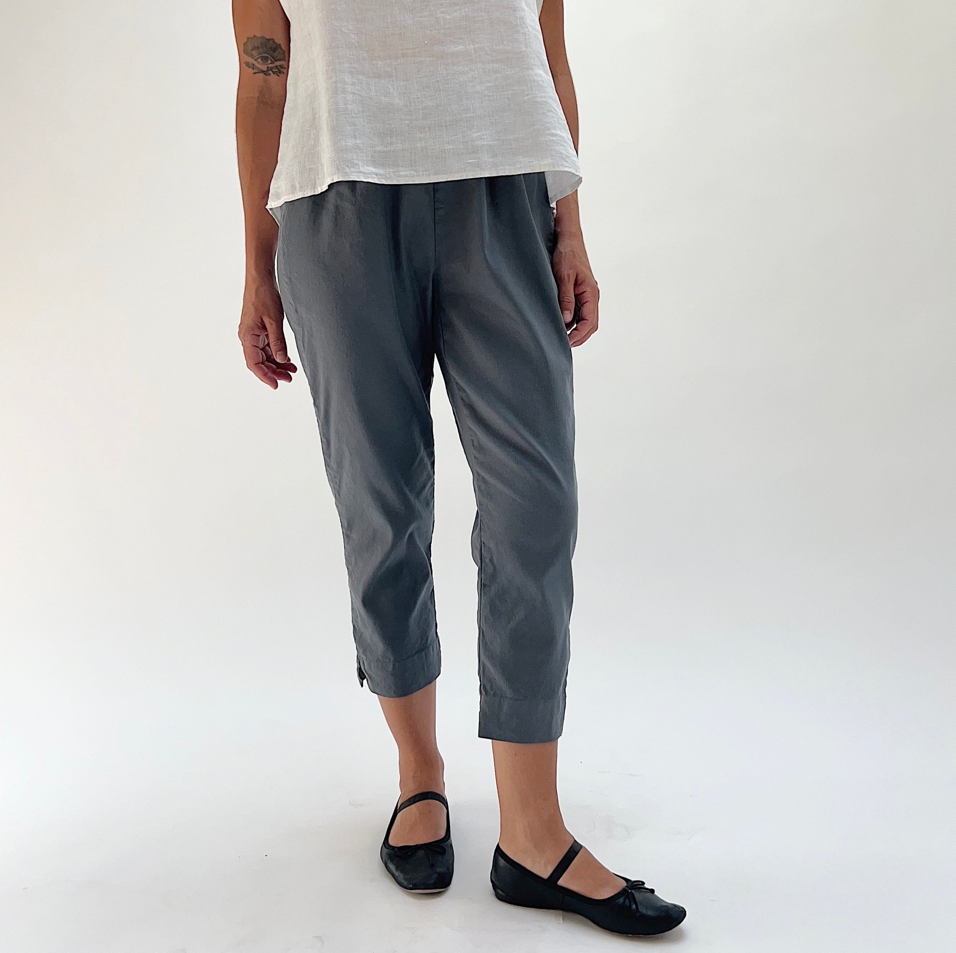 Front view of model wearing Cut Loose iron grey linen-Tencel taper crop pant, showing elastic waistband, tapered leg, side seam vent, and mid-calf cropped length