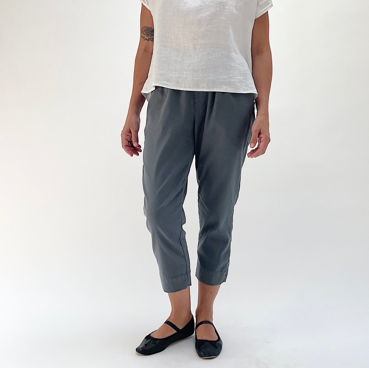 Full front view of model wearing Cut Loose linen-Tencel crop pant in iron, showing charcoal grey color, elastic waist, and tapered leg narrowing at the ankle