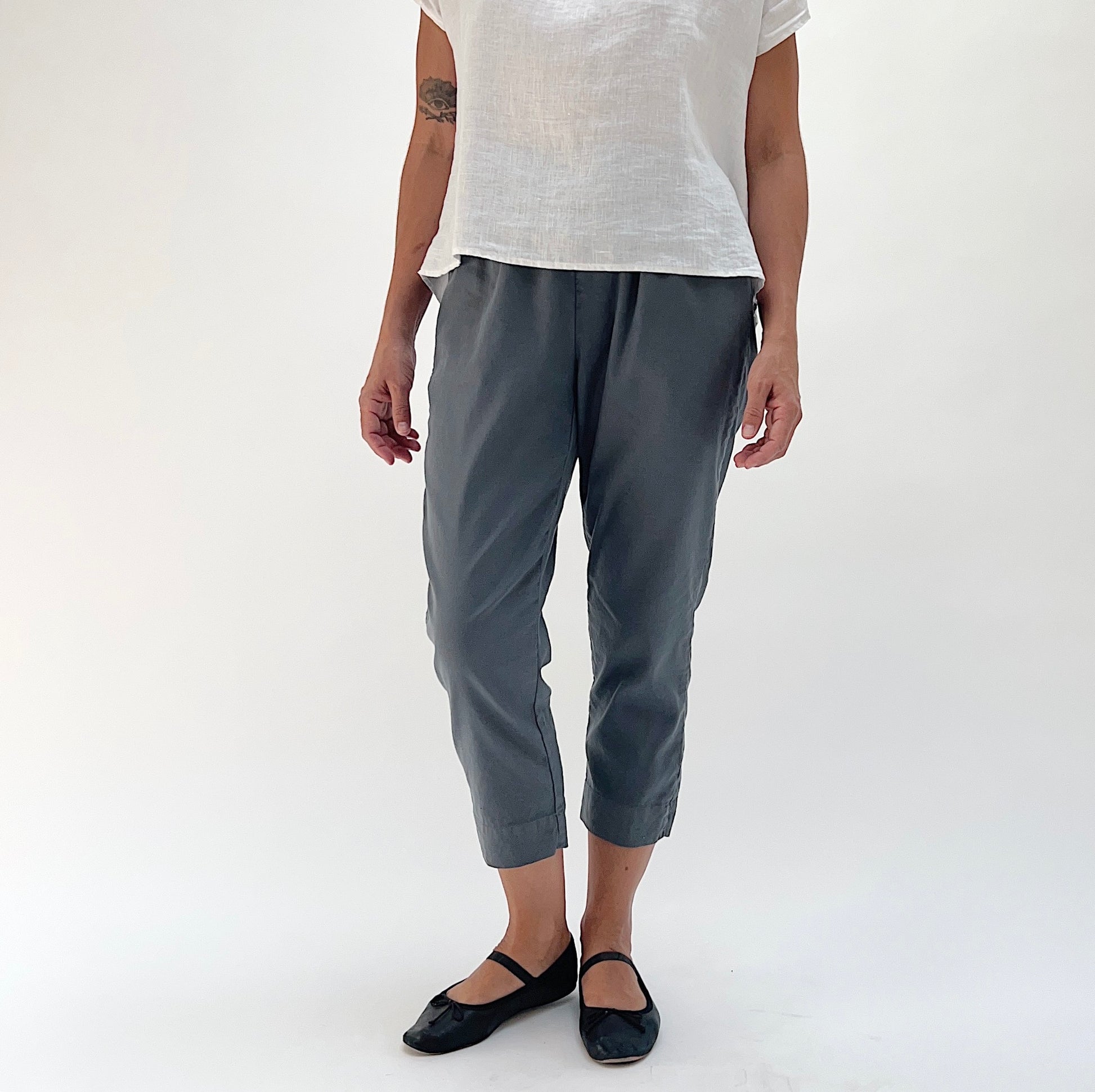 Full front view of model wearing Cut Loose linen-Tencel crop pant in iron, showing charcoal grey color, elastic waist, and tapered leg narrowing at the ankle
