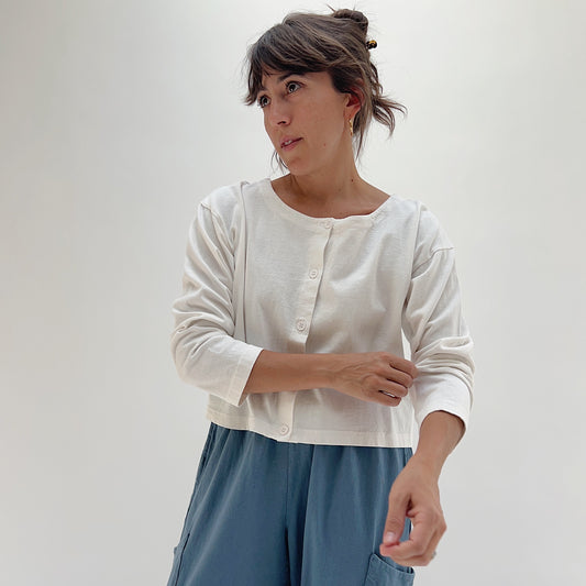 Three-quarter front view of model wearing Pacific Cotton cream long sleeve button-front shirt, showing crew neckline, center button placket, and relaxed cropped fit