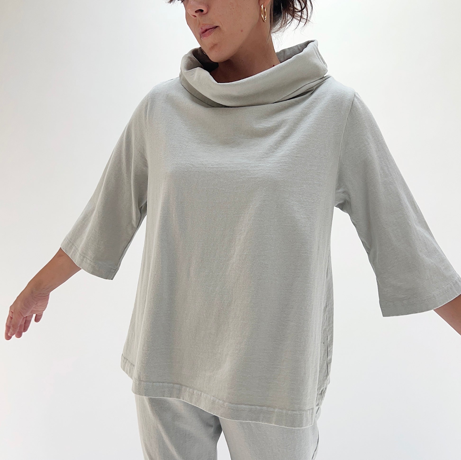 Three-quarter front view of model wearing Bryn Walker orlaya 3/4 sleeve Etta top, showing draped cowl neckline, 3/4 sleeves, boxy A-line silhouette, and sage green color