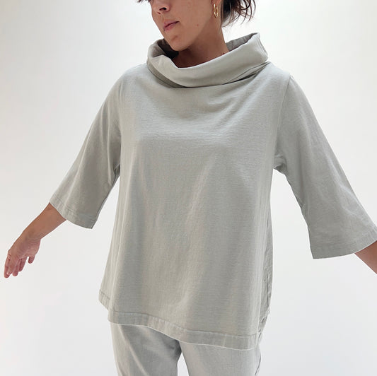 Three-quarter front view of model wearing Bryn Walker orlaya 3/4 sleeve Etta top, showing draped cowl neckline, 3/4 sleeves, boxy A-line silhouette, and sage green color