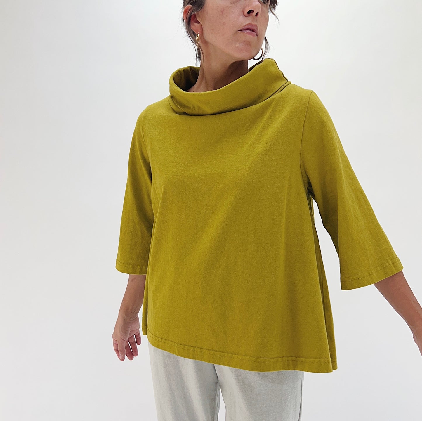 Three-quarter front view of model wearing Pacific Cotton chartreuse 3/4 sleeve Etta top, showing draped cowl neckline, boxy A-line silhouette, 3/4 sleeves, and banded hem

