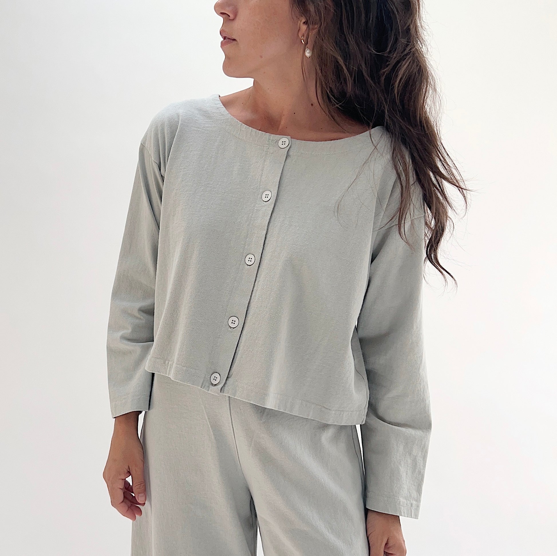 Close front view of model wearing Pacific Cotton orlaya long sleeve button front shirt, showing crew neckline, center button placket, long sleeves, and relaxed cropped boxy fit