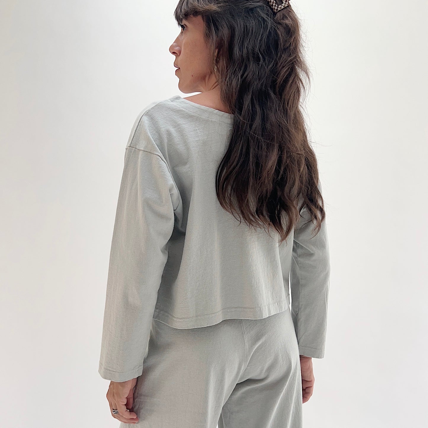Back view of model wearing Pacific Cotton orlaya long sleeve button front shirt, showing relaxed cropped boxy silhouette, long sleeves, and straight hem