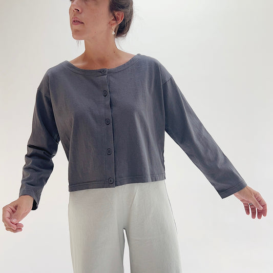 Three-quarter front view of model wearing Pacific Cotton moonlight long sleeve button front shirt, showing wide neckline, five-button center placket, long sleeves, boxy cropped fit, and slate blue-grey color