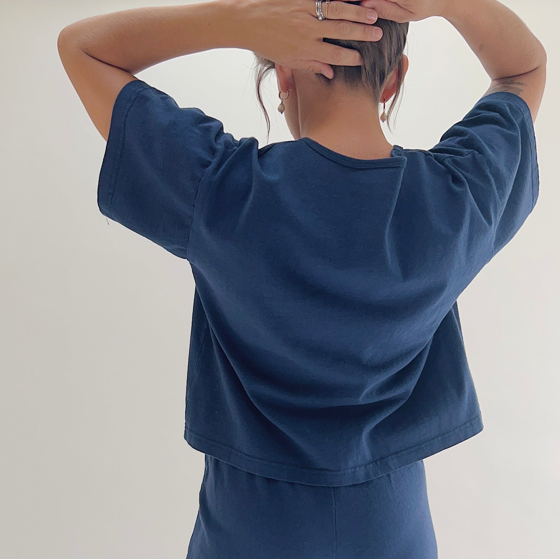 Back view of model wearing Pacific Cotton nova crop crew tee, showing crew neckline, short sleeves, boxy cropped silhouette, banded hem, and deep teal color