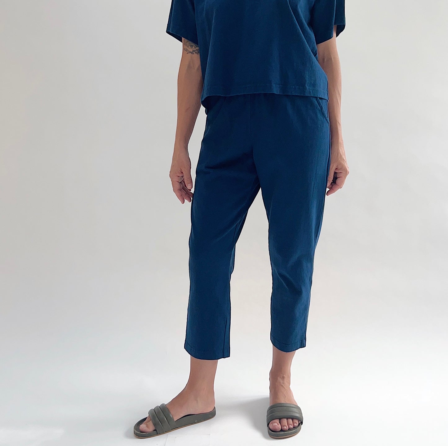 Front view of model wearing Pacific Cotton nova sunday pant with hands in pockets, showing elastic waistband, side pockets, straight cropped leg, and deep teal color, styled with matching nova crop crew tee

