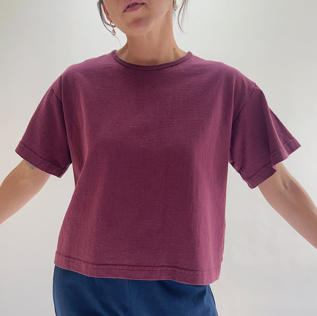 Close front view of model wearing Pacific Cotton rhone crop crew tee, showing ribbed crew neckline, short cuffed sleeves, boxy cropped fit, banded hem, and berry plum color

