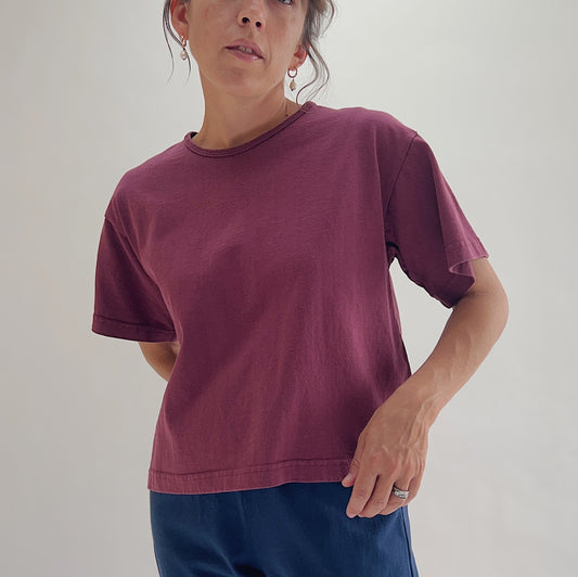 Three-quarter front view of model wearing Pacific Cotton rhone crop crew tee, showing crew neckline, short cuffed sleeves, boxy cropped silhouette, and berry plum color
