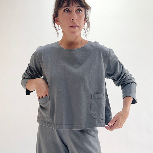 Full front view of model wearing Pacific Cotton dolomite boxy shirt with hands in pockets, showing crew neckline, two front patch pockets, long sleeves, boxy cropped fit, and washed slate grey color, styled with matching dolomite pants