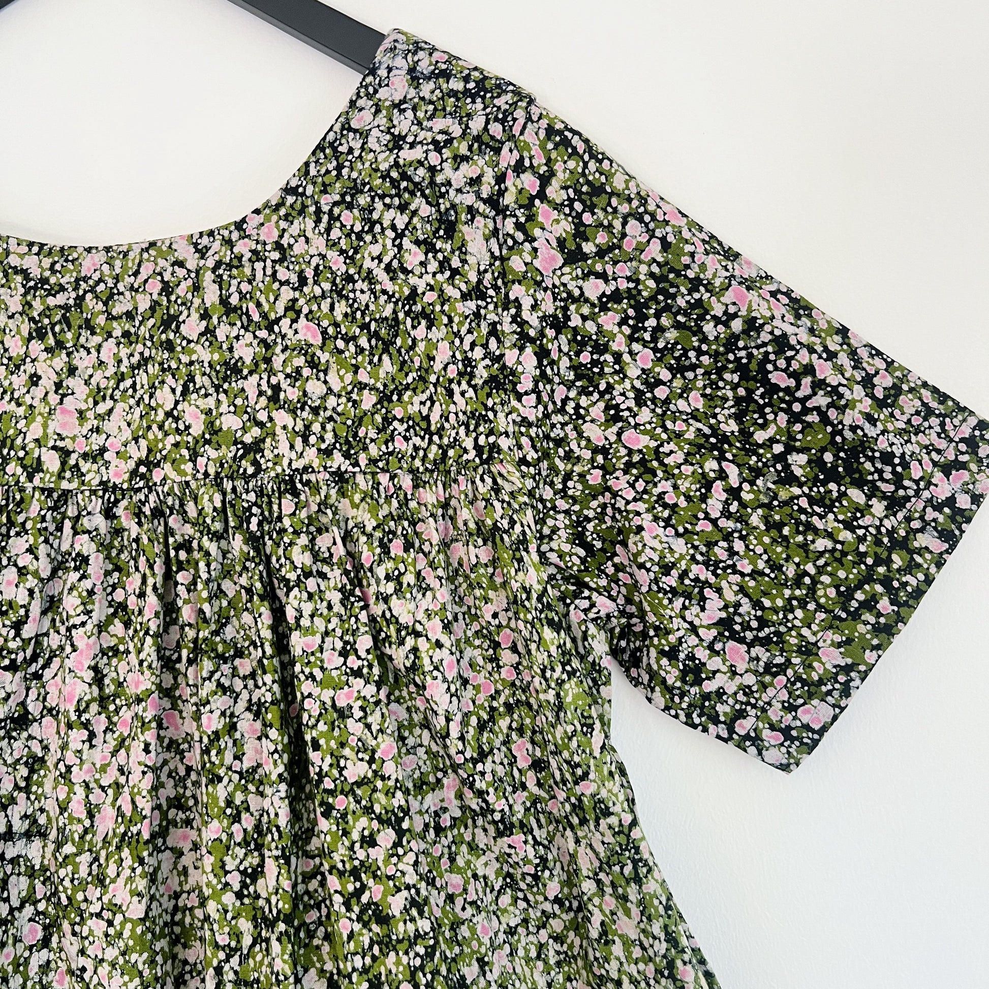 Close-up of the upper bodice and sleeve of the Sakina Dress in Green and Pink Speckle, highlighting the round neckline, gathered yoke seam, short sleeve hem, and hand-printed green, pink, and white speckle pattern on dark navy Batiki cotton with natural dye variation

