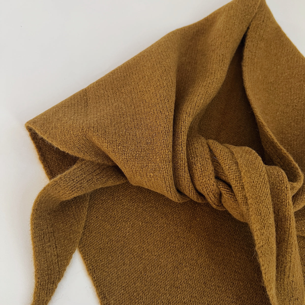 Close-up of the Winter Olive merino wool scarf showing its knit texture, loose knot and pointed ends.
