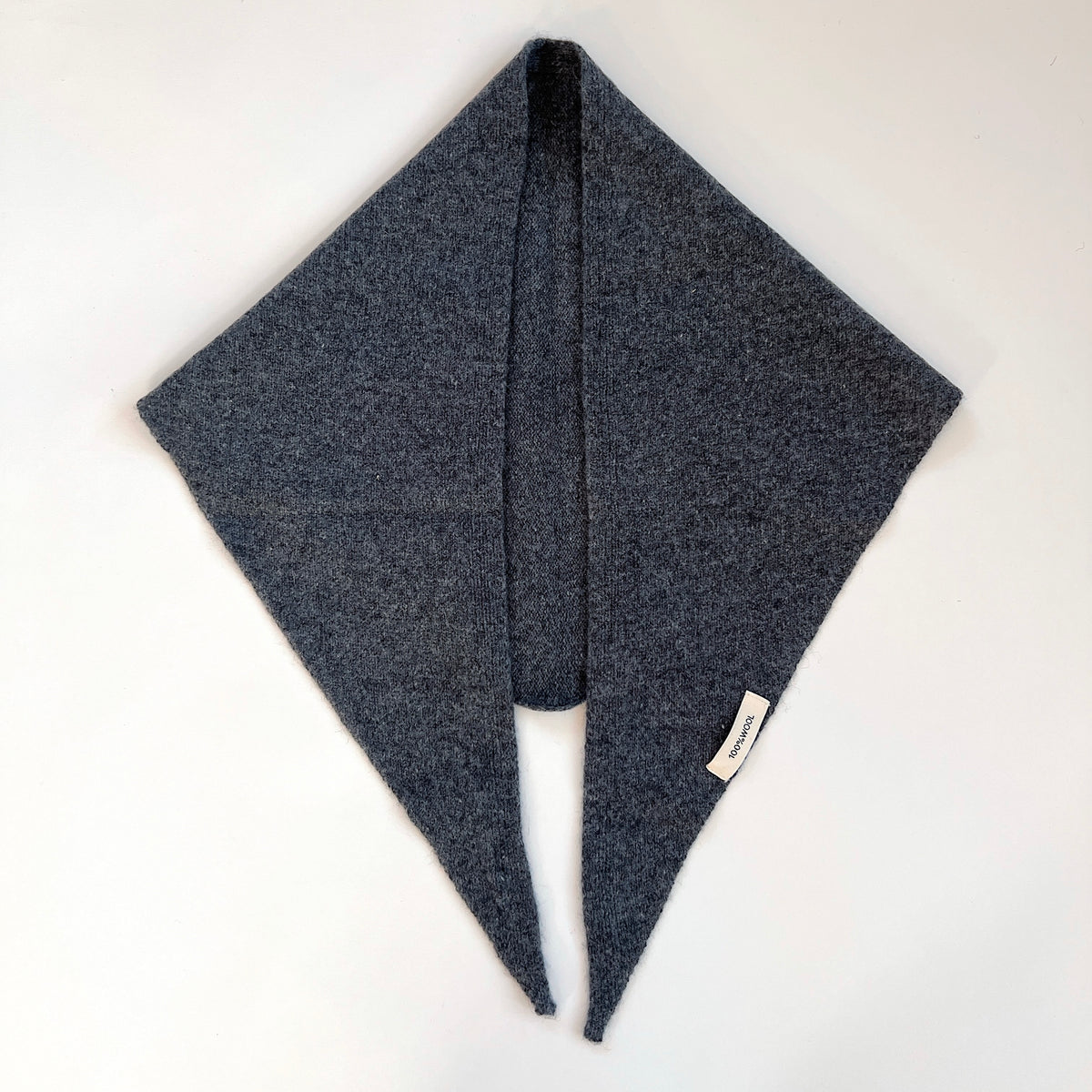 Flat lay view of the Charcoal merino wool triangle scarf with its long pointed ends hanging side by side.
